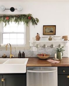 a kitchen with black cabinets, white walls and wooden counter tops is decorated with greenery