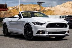 a white mustang convertible parked in a parking lot next to other cars and construction equipment