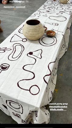 a long table covered in white cloth with designs on it and a vase sitting on top