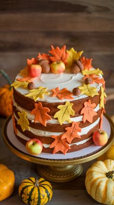 a multi layer cake decorated with fall leaves and acorns on a gold plate