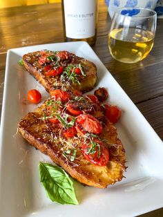 two pieces of bread on a plate with tomatoes and basil next to a glass of wine