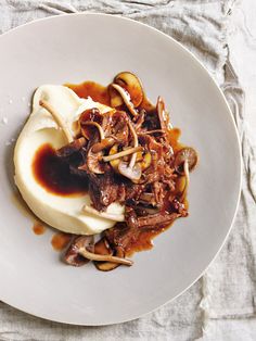 a white plate topped with meat and vegetables covered in gravy on top of a table