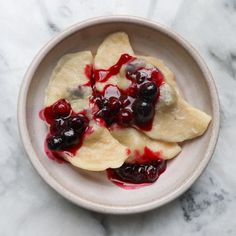 two crepes with blueberry sauce in a white bowl on a marble surface