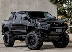 a black toyota truck parked in front of a concrete wall with trees and bushes behind it