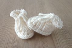 two white knitted baby booties sitting on top of a wooden floor