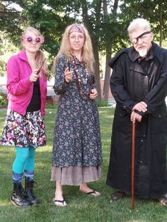 three people dressed up in costumes and holding umbrellas standing on grass with trees behind them