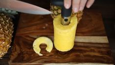 a person cutting up a pineapple on top of a wooden cutting board with a knife