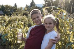 two young children standing in front of a corn field holding a jar of peanut butter