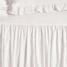 the bed is made with white linens and ruffled bedspread on it