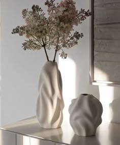 two white vases with flowers in them on a table