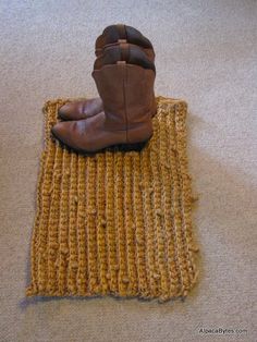 a pair of brown boots sitting on top of a yellow floor mat next to a white wall