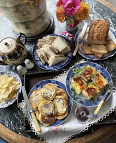 a table topped with plates of food next to a vase filled with flowers and bread