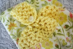 a yellow crocheted flower on top of a white lace doily with a button