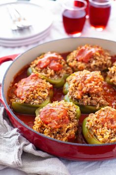 stuffed peppers with meat and rice in a red pan on a table next to glasses of wine