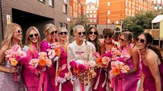 a group of women standing next to each other wearing pink dresses and holding bouquets