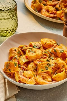 a bowl filled with pasta and shrimp next to a glass of green wine on a table