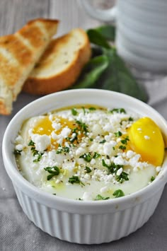 a white bowl filled with eggs and cheese next to some slices of bread on a table