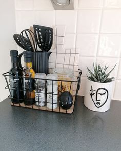 a kitchen counter with utensils and bottles in a basket next to a potted plant