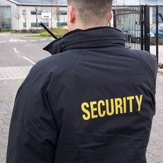 a security man standing in front of a gate with his back turned to the camera