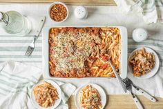 a casserole dish on a table with two bowls of pasta and other dishes