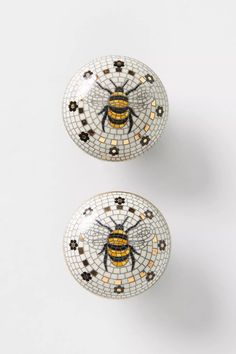 two decorative bees sitting on top of each other in front of a white wall with black and yellow designs