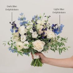 a bouquet of white and blue flowers is being held by someone's hand in front of a wall