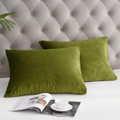 two green pillows sitting on top of a bed next to a cup and saucer