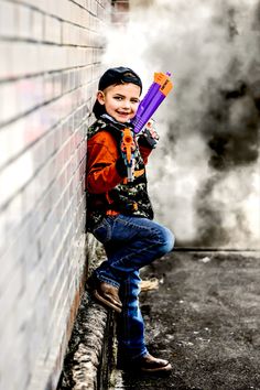 a young boy is holding an item in his hand while leaning against a brick wall