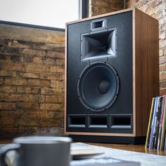 a large speaker sitting on top of a wooden table next to a brick wall and bookshelf