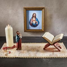 an open book sitting on top of a rug next to a candle and statue in front of a painting