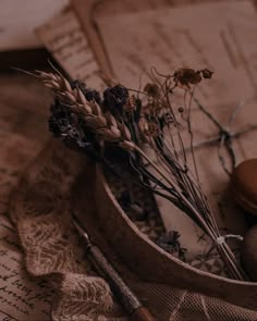 dried flowers in a wooden bowl on top of an old book with scissors and writing utensils