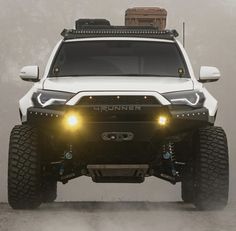 the front end of a white truck with its lights on and foggy sky in the background