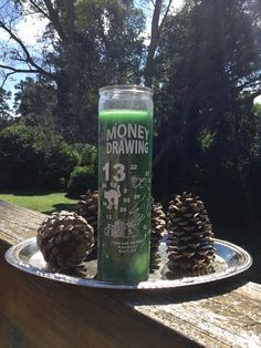 a bottle of money drawing next to some pine cones on a metal platter with a tree in the background