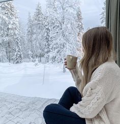 a woman sitting in front of a window holding a coffee cup and looking out the window