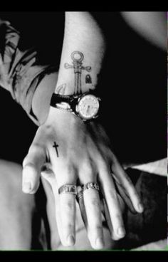 black and white photograph of two hands holding each other with cross tattoos on them,