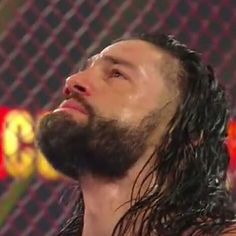 a man with long hair and beard standing in front of a chain link fence looking up at the sky