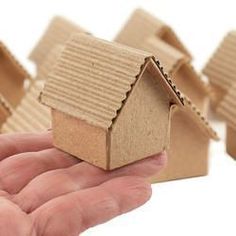 a hand holding a small model house in front of smaller houses that are lined up on top of each other