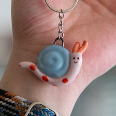 a hand holding a keychain with a snail charm on it's wrist