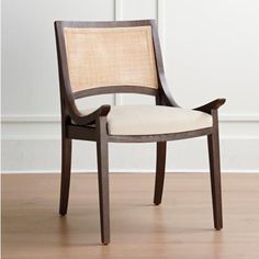 a wooden chair with a beige seat and back cushion on a hard wood floor in front of a white wall