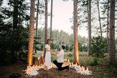 a man kneeling down next to a woman in front of trees with candles on them