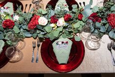 the table is set with red and white flowers, silverware, and napkins