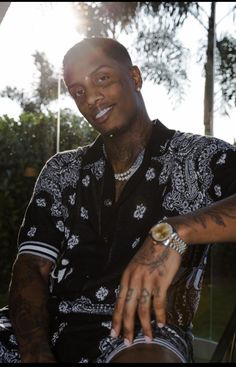 a man with tattoos on his arm and wrist sitting in a chair smiling at the camera