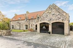 an old stone house with two garages and brick driveway in the middle of it