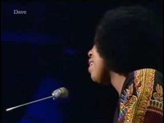 a man with an afro standing in front of a microphone and wearing a colorful shirt