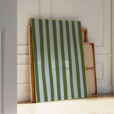 a green and white striped wall hanging next to an open bookcase on the floor