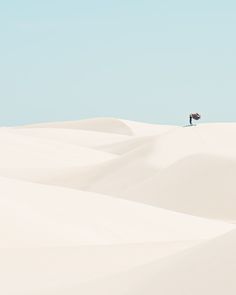 a lone person standing on top of a large white sand dune in the middle of nowhere