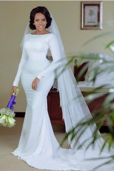 a woman in a white wedding dress holding a bouquet and posing for the camera with her veil draped over her head