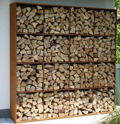 a large stack of firewood sitting on top of a sidewalk next to a green trash can