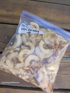 a plastic bag filled with sliced bananas on top of a wooden table next to an apple pie filling