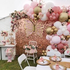 an outdoor party with balloons and flowers on the wall, table set up for a baby's first birthday